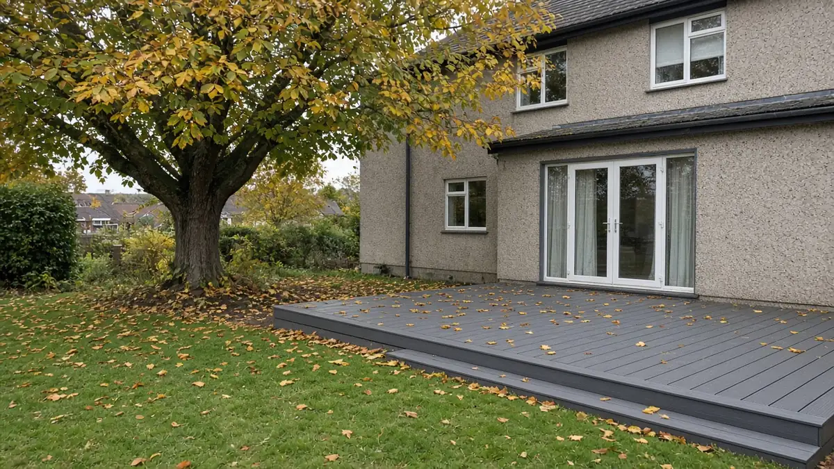 Example image: slate-grey composite deck with autumn leaves beneath a large tree behind a 1930s semi
